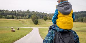 father-carrying-his-son-on-shoulders-hiking-down-the-road-on-a-picture-id1176545296.jpg