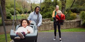 two mum friends pushing their kids on swing in park