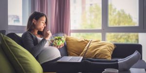 pregnant woman eating salad on sofa 