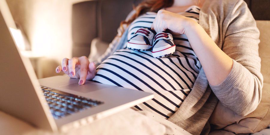 pregnant woman holding baby shoes whilst shopping online