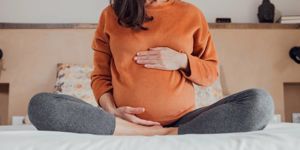 pregnant woman sat on bed holding bump