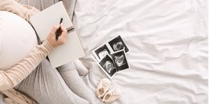 Pregnant woman writing baby names in notebook