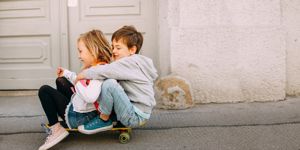 brother and sister sitting on skateboard rolling down hill