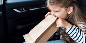 little girl being sick into bag in car