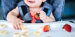 smiling baby in high chair with fruit