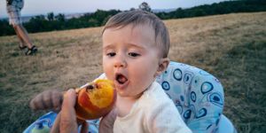 baby in high chair eating peach fruit