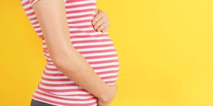 closeup-view-of-pregnant-woman-touching-belly-on-yellow-background-picture-id948948394.jpg