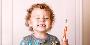 toddler-smiling-while-holding-a-toothbrush-picture-id184111089.jpg
